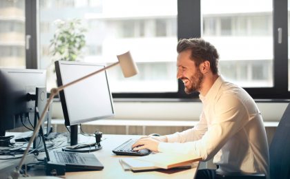 Man smiling at computer doesn't have cyber liability insurance.