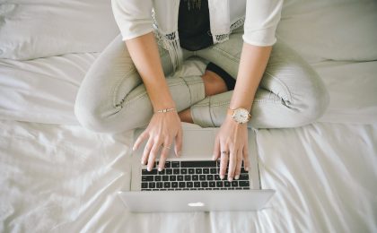 Woman typing on laptop on bed.