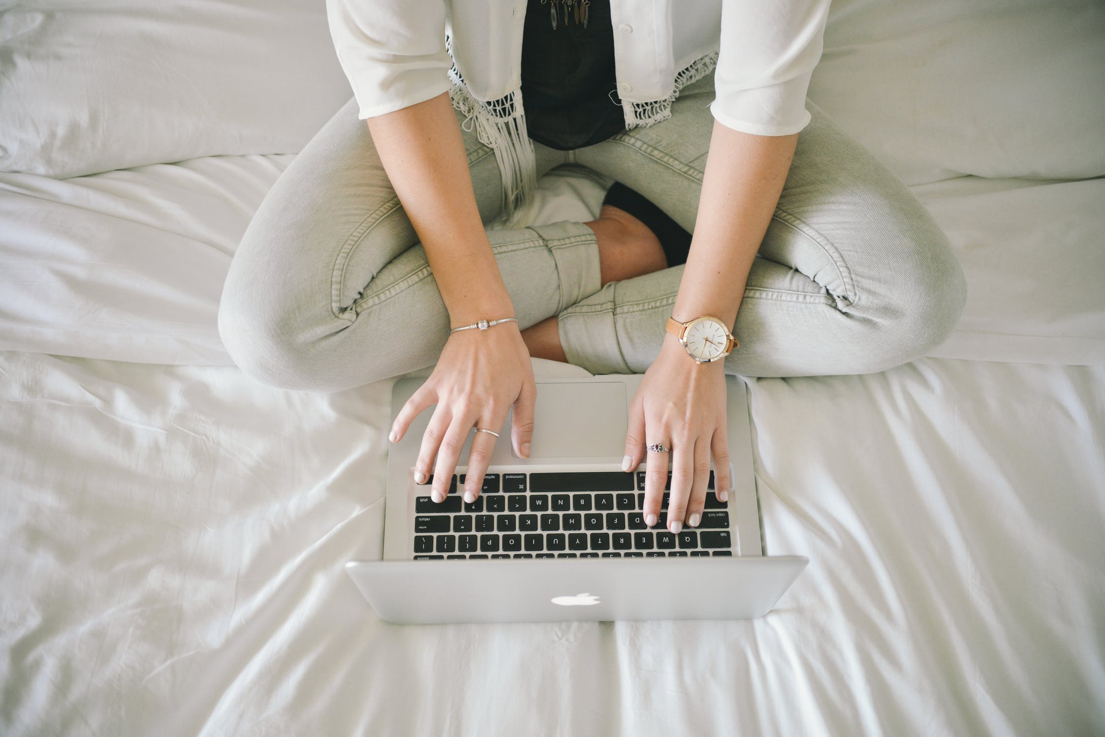 Woman typing on laptop on bed.