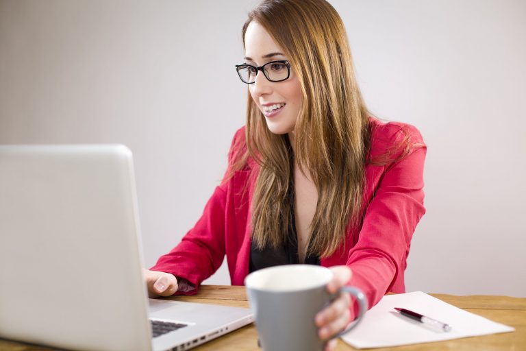 Woman in glasses at laptop with coffee.