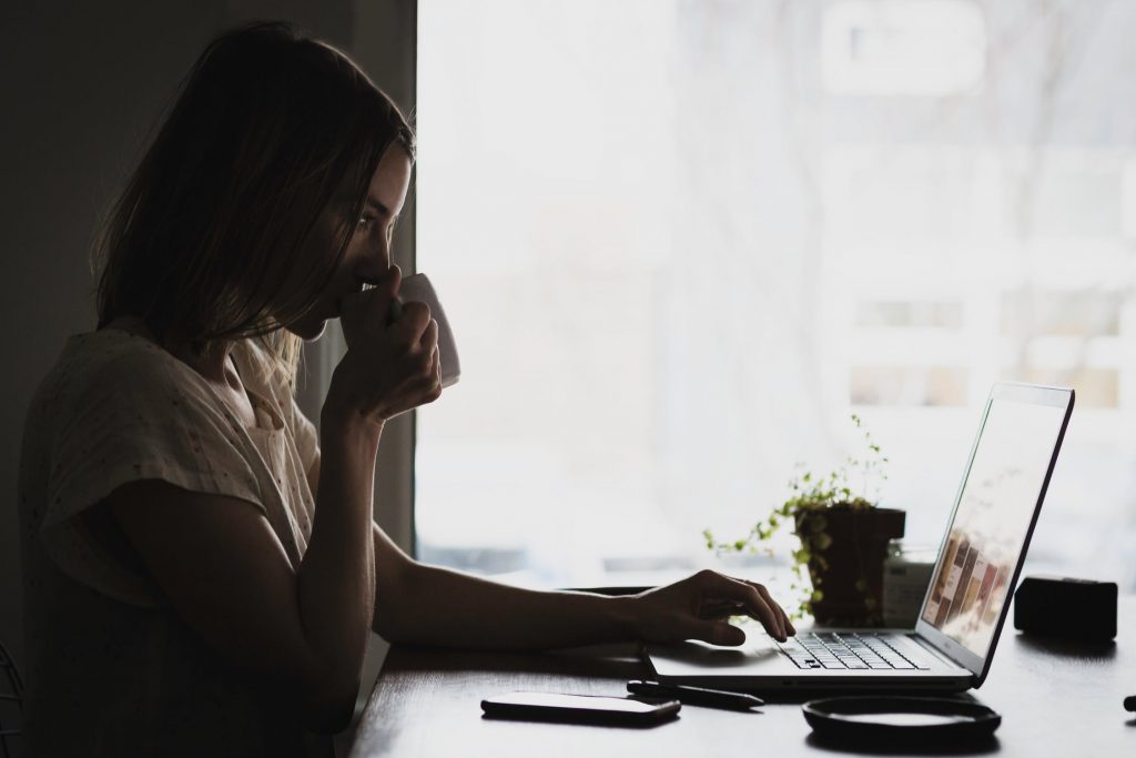 Woman drinking coffee getting online quote on her laptop.