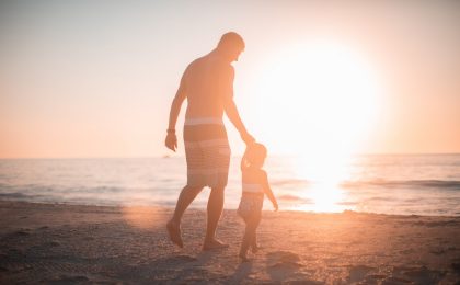 Man holding child's hand at beach.