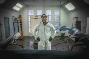 Man standing in painting gear with auto parts.