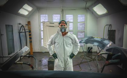 Man standing in painting gear with auto parts.