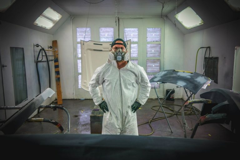 Man standing in painting gear with auto parts.