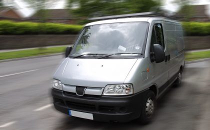 Silver van with commercial auto insurance driving down a road.